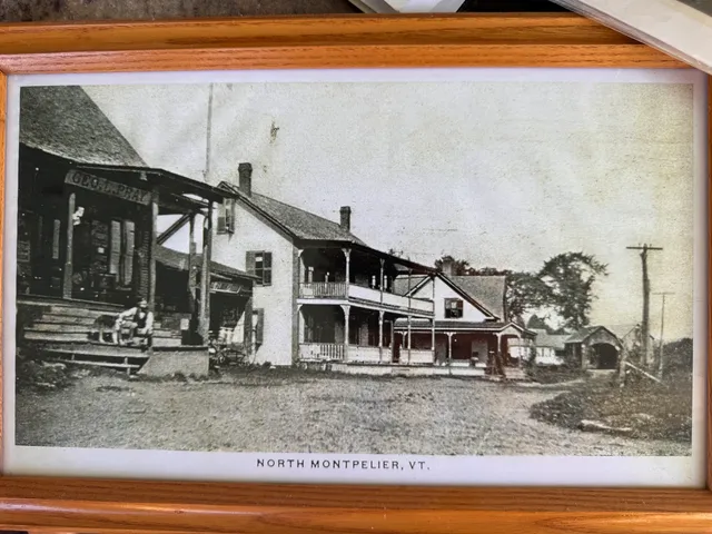 Postcard of the "Geo. J. Pray" storefront and an inn, with a man and his dog sitting on the porch steps.