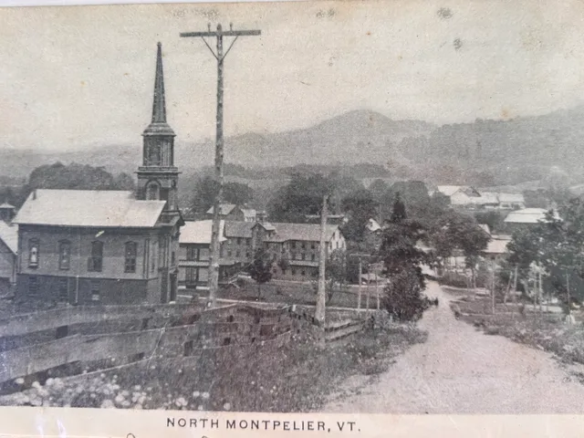 Panoramic postcard of North Montpelier village with the church steeple, mill buildings, and mountains beyond.
